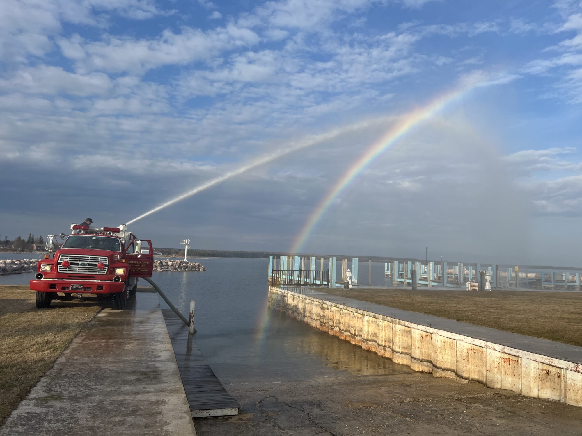 Fire truck spraying water creates rainbow over lake.